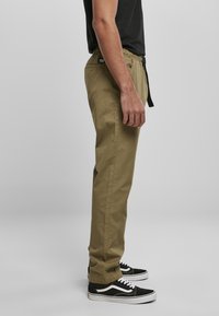 Pantalones caquis con cintura elástica, diseño de pierna recta y bolsillos laterales. Combinados con zapatillas negras con acentos blancos.