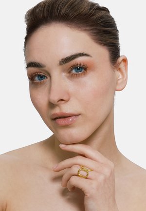 Goldring mit einem verwundenen Design, das eine ovale und eine runde Form zeigt. Die Hand des Models ruht unter dem Kinn und präsentiert den Ring.