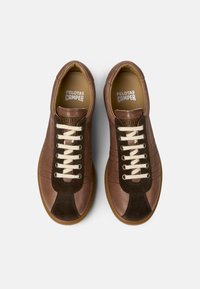 Zapatillas deportivas de cuero marrón con puntera de ante marrón oscuro, cordones crema y suela de goma estriada. Presentan un logotipo en relieve en la lengüeta.