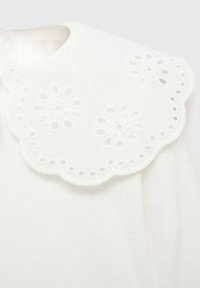 Valkoinen vaate, jossa on hampaanreunainen kaulus, joka on koristeltu monimutkaisilla kukkaleikkauksilla. Pehmeä tekstuuri, jossa on sileä pinta.