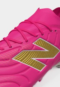 Scarpino da calcio rosa acceso con logo dorato, stringhe rosa e design testurizzato su sfondo bianco.