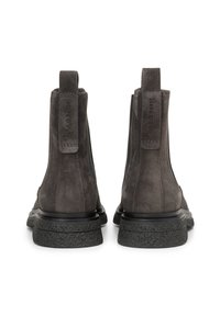 Bottes à chevilles en suède gris avec une semelle en caoutchouc noir plat, des languettes à l'arrière et un détail de marque embossé sur le côté. Texture lisse.