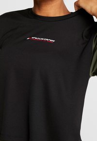 Svart atletisk t-shirt med korta ärmar och gröna detaljer, rund hals och en liten röd och vit "TOMMY SPORT" logotyp på framsidan.