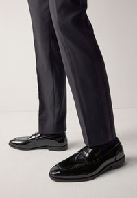 Sorte loafers i laklæder med syningsdetaljer, lav hæl og blank finish, kombineret med mørke, skræddersyede bukser.