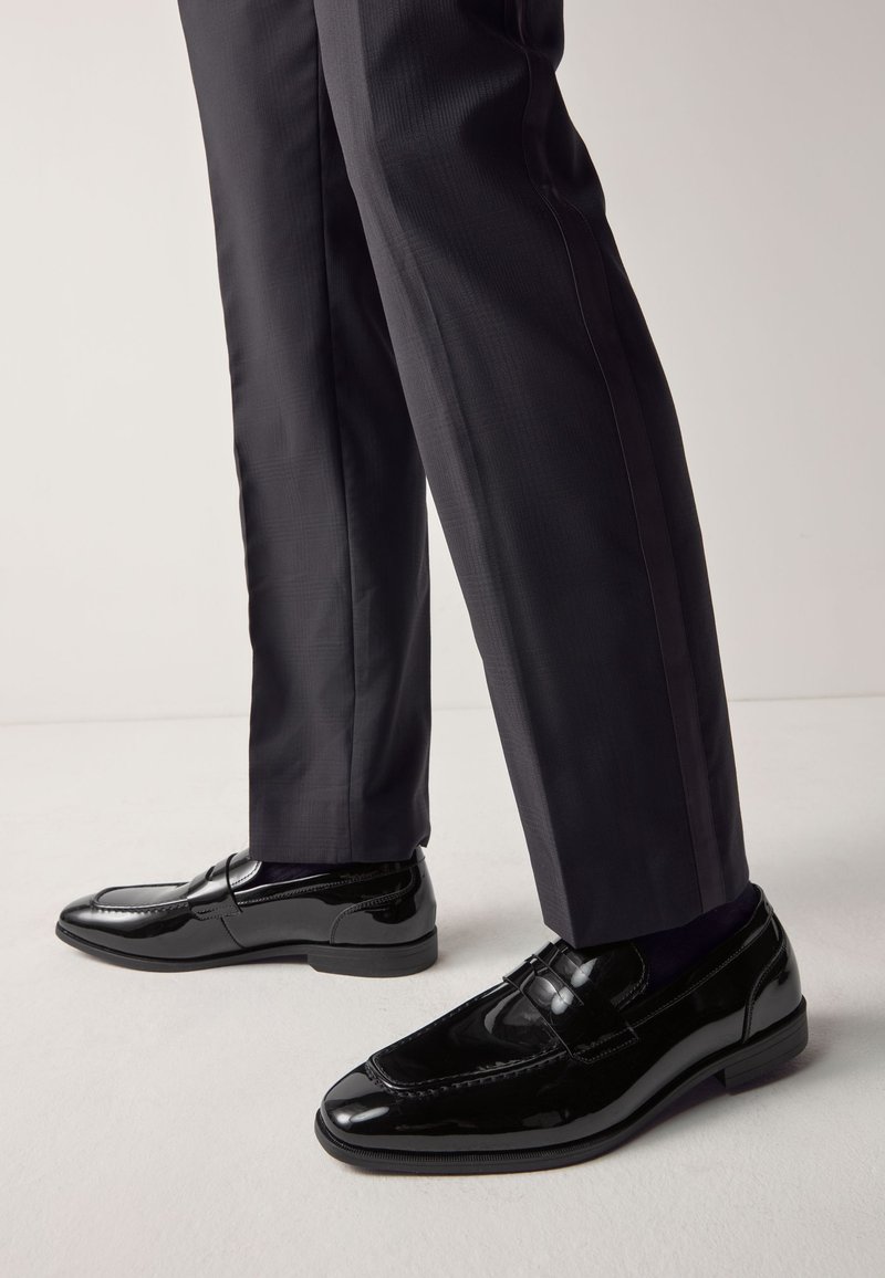 Sorte loafers i laklæder med syningsdetaljer, lav hæl og blank finish, kombineret med mørke, skræddersyede bukser.