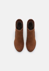 Stivaletti alla caviglia in suede marrone con punte arrotondate, pannelli laterali elastici e fodera morbida. Il design presenta hardware minimal e una silhouette slanciata.