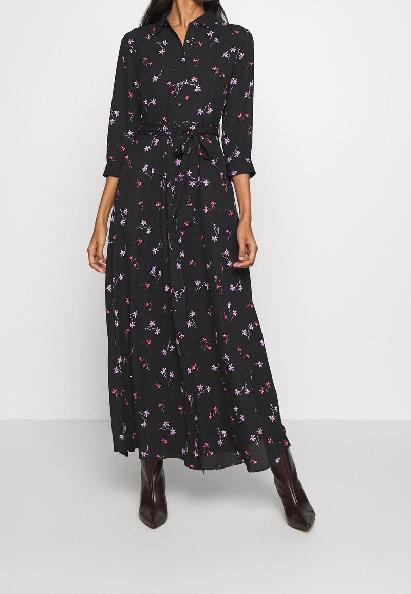 Zwart langemouwige jurk met bloemenpatronen in roze en paars, ceintuur in de taille en een zwierige rok. Gemaakt van een lichte, zachte stof.