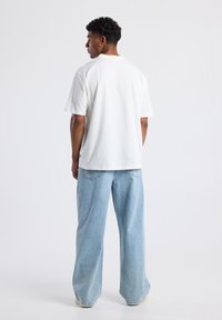 White short-sleeve t-shirt with a relaxed fit, paired with light blue wide-leg jeans. Cotton fabric with a smooth texture.