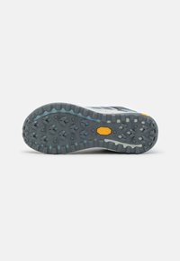 Suola di scarpa da trail running gray e bianca con una superficie in gomma testurizzata, caratterizzata da un logo Vibram e da tasselli a forma di piramide per una migliore aderenza.