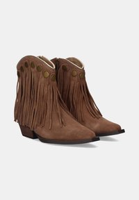 Botas de tobillo de ante marrón con flecos a los lados, con parte superior redondeada y acentos de botones de latón. Tacón bajo y apilado y punta afilada.