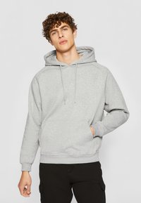 Sudadera gris con capucha hecha de tela suave, con un bolsillo tipo canguro, puños acanalados y un corte holgado. Sin patrones ni acentos visibles.
