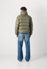 Oliven grønn pufferjakke med hette, med quiltet design og myk tekstur, kombinert med lyseblå baggy denimjeans.