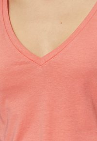 Koralowa koszulka z dekoltem w serek, wykonana z miękkiego, lekkiego materiału; charakteryzuje się gładką teksturą i subtelnym połyskiem, idealna na codzienne noszenie.