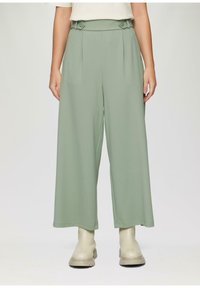 Brede broek van zacht, lichtgroen stof. Kenmerkt zich door een hoge taille met dubbele knopen en voorplooien. Gepaard met beigerode enkellaarsjes.