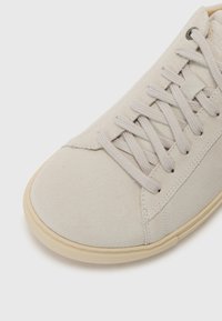Lys beige ruskinnsneakers med rund tå, flate lisser og gummisåle. Har subtile stingdetaljer og minimalistisk design.