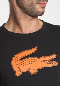 Black cotton t-shirt featuring a large orange crocodile graphic with triangular patterns. Round neck design. Smooth texture.