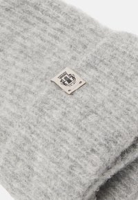 Gray knitted scarf with a textured pattern and a small beige tag featuring a logo, stitched into the fabric. Soft, warm material.
