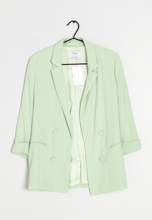 Blazer verde claro con un ajuste ligeramente sobredimensionado, que cuenta con dos bolsillos delanteros, mangas remangadas y cierre de doble botón. Textura de tela simple.