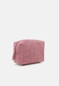 Trousse de maquillage en velours côtelé rose de forme rectangulaire, avec une fermeture à glissière et des rayures verticales texturées. Équipée d'une poignée latérale pour faciliter le transport.
