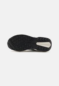 Suola di scarpe da corsa con superficie in gomma nera rugged e battistrada triangolare, con un accento bianco. Branding visibile sulla intersuola.