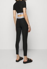 Svart kort topp och högmidjade leggings med vita sidostycken. Materialet verkar elastiskt. Svarta sandaler med tjocka sulor och metalldetaljer.