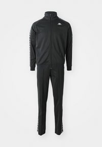Ensemble de survêtement noir zippé intégral avec logo blanc sur la poitrine, bandes blanches de marque sur les manches et les jambes de pantalon, et poignets côtelés aux manches.
