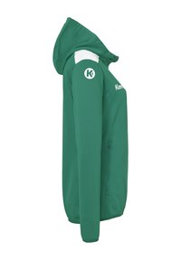Grøn hættejakke lavet af blødt stof, med en hvid accent på skulderen, lynlåslommer og et logo på ærmet.