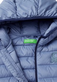 Ljusblå puffy-jacka med huva, med sydda sektioner och en grön logotags. Slät, glänsande textur med dragkedjestängning.