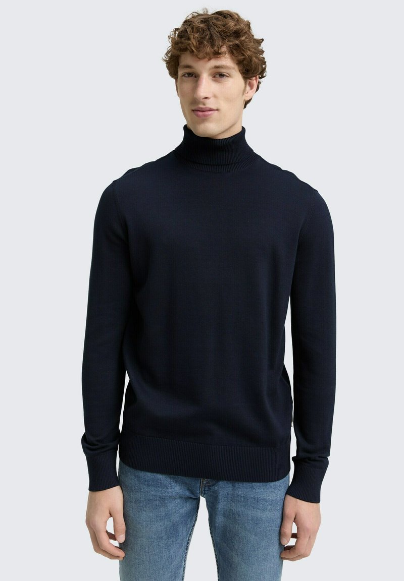 Tumed meresinine polo-sweater, millel on soonikuga kaelus ja varrukad, valmistatud tekstuuriga kudumifast, koos helesiniste teksadega.
