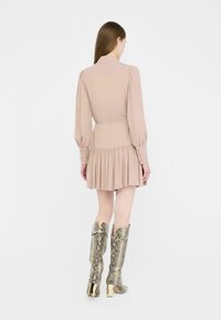 Abito rosa chiaro con maniche a sbuffo e gonna a pieghe, abbinato a stivali alti in pelle di serpente metallizzata con tacco dorato.