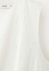 Blouse blanche sans manches avec broderie ajourée fleurie et col en V, étiquetée MNG, fabriquée en Europe.
