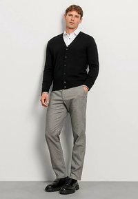 Schwarzer gestrickter Cardigan mit rundem Ausschnitt und Knöpfen, kombiniert mit grauer Hose und schwarzen Schuhen. Glatte Textur und maßgeschneidertes Design.