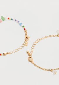 Δύο βραχιόλια: το ένα με πολύχρωμες χάντρες και χρυσά εξαρτήματα, το άλλο αλυσίδα χρυσού με ένα μικρό διάφανο φιλέτο.