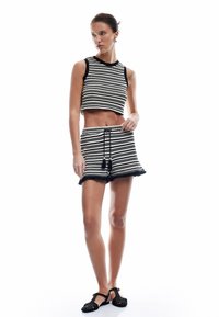 Zwart-wit gestreepte gebreide crop top met ronde halslijn en bijpassende shorts met gerafelde randen. Zwarte bandjeschoenen maken de look compleet.