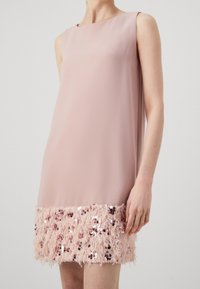 Robe sans manches élégante en tissu rose pâle, avec un ourlet inférieur texturé orné d'accents duveteux et de paillettes dispersées pour plus de détails.