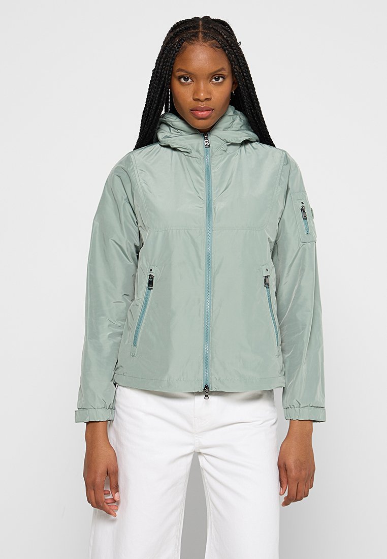 Hellgrüne, leichte Jacke mit Kapuze, Frontreißverschluss und zwei Seitentaschen. Verfügt über elastische Bündchen und eine kleine Taschen am Ärmel.
