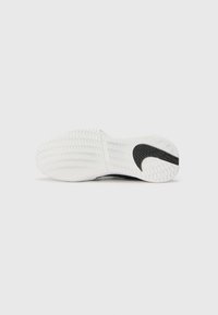 Valkoiset tennarit, joissa on teksturoitu sahalaitakuviollinen pohja, musta Nike-logo ja kaareva muotoilu sivussa, joka tarjoaa pitoa ja kitkaa.