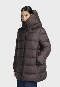Giacca a vento imbottita di colore marrone scuro, con colletto alto, chiusura con zip frontale e tasche laterali. Design imbottito con una texture liscia.