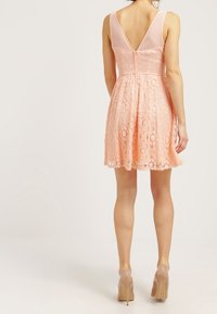 Růžová krajková šaty s přiléhavým korzetem a sukni ve tvaru A. Průhledný panel na V vzadu. Dokončeno texturovaným květinovým vzorem.