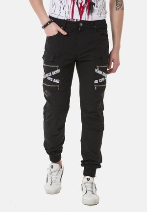 Black cargo pants made of synthetic material with zippered pockets and white text accents, featuring ankle cuffs for a tapered fit.