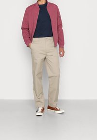 Lekka różowa kurtka bomberka, granatowy T-shirt, beżowe spodnie i brązowe niskie trampki. Wyposażona w zamki i klasyczny krój.