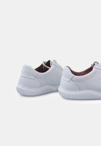 White leather sneakers featuring perforated detailing, rounded toe, and textured rubber sole with horizontal ridges. Laces are included.