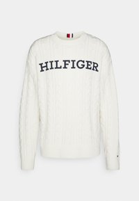 Weißer Kabelstrickpullover mit gerippten Bündchen und Saum. Mit dem "HILFIGER"-Logo in Marineblau über der Brust und kontrastierenden roten und marineblauen Akzenten im Nacken.