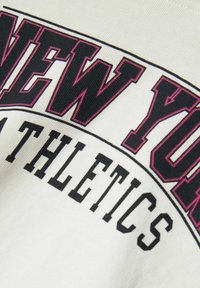 Felpa bianca in cotone con audace design del testo "NEW YORK ATHLETICS" in nero e rosa, con una finitura testurizzata e scritte arcuate.