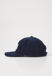 Marine corduroy pet met een gebogen rand, verstelbare band en een rechthoekig label aan de voorkant. Gelaagd stof met zichtbare lijnen.