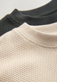 Kolme neuleen kaulusta kerma, musta ja beige. Teksturoitu neule ja ribatut hihat, joissa on vaihtelevaa kuvastoa ja värejä visuaalista kontrastia varten.