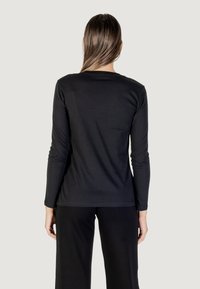 Maglietta nera a maniche lunghe realizzata in tessuto morbido, con scollo rotondo e design minimalista, abbinata a pantaloni neri larghi.