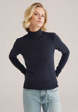 Navyblauer Rollkragenpullover aus weichem Strickstoff, mit langen Ärmeln, gerippten Bündchen und Saum, kombiniert mit hellen Jeans.