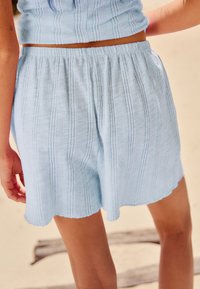 Șorturi albastre deschise din bumbac cu un model texturat, având o talie elastică și marginile tivite în formă de valuri la poale.