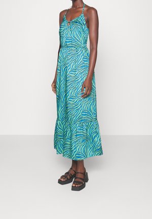 Robe maxi sans manches à imprimé zèbre bleu et vert avec ourlet à volants, portée avec des sandales plateforme noires, sur une personne debout.
